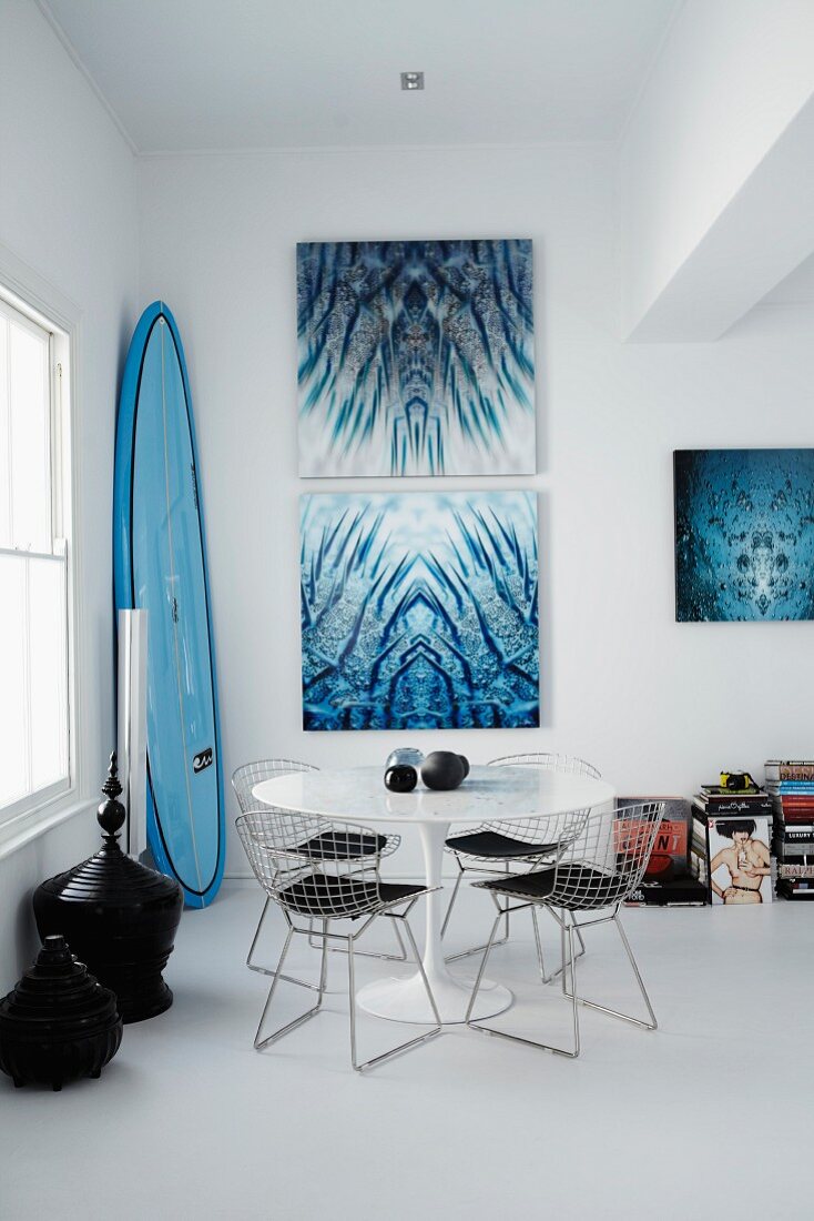 Classic wire-framed chairs around Tulip table in dining room; artworks with water motifs on wall and surfboard