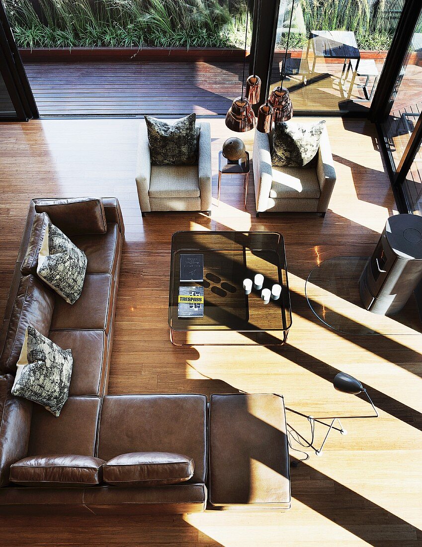View down onto brown leather corner couch in penthouse apartment with glass facade and adjoining terrace