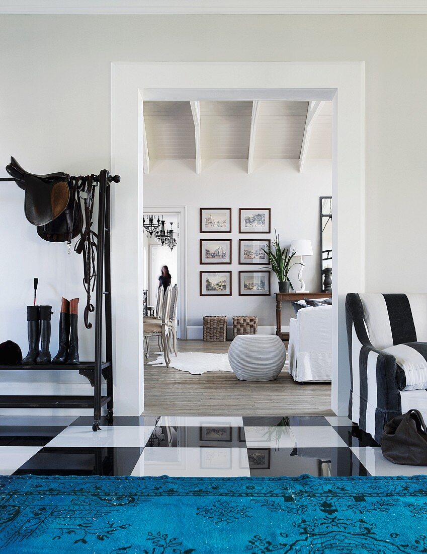 Blick vom Eingangsbereich mit glänzendem Schachbrettmuster Fliesenboden und blauem Teppich in offenen Wohnbereich im eleganten Landhausstil