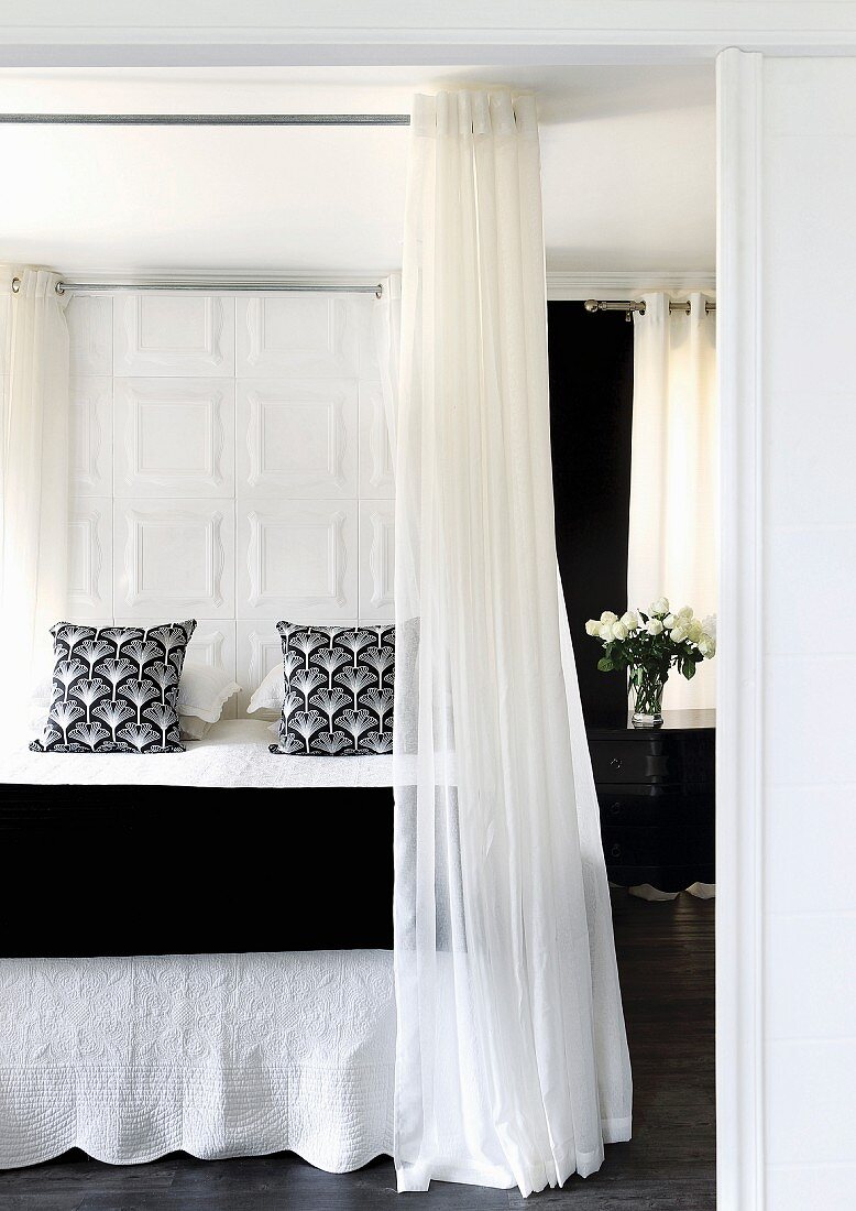 Elegantes Doppelbett mit schwarz-weissen Textilien und raumhoher Vorhang an umlaufender Stange