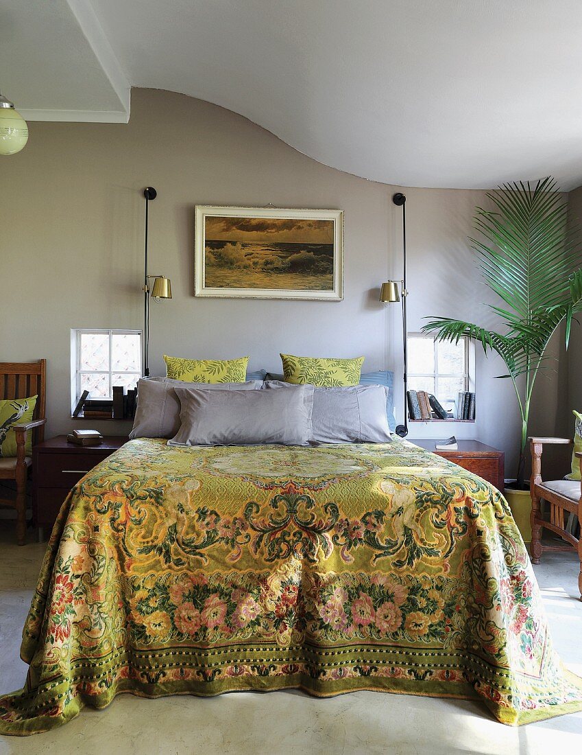 Bettüberwurf in traditionellem Ornament- und Blumenmuster auf Doppelbett vor grau getönter Wand und geschwungene Decke in Schlafzimmer