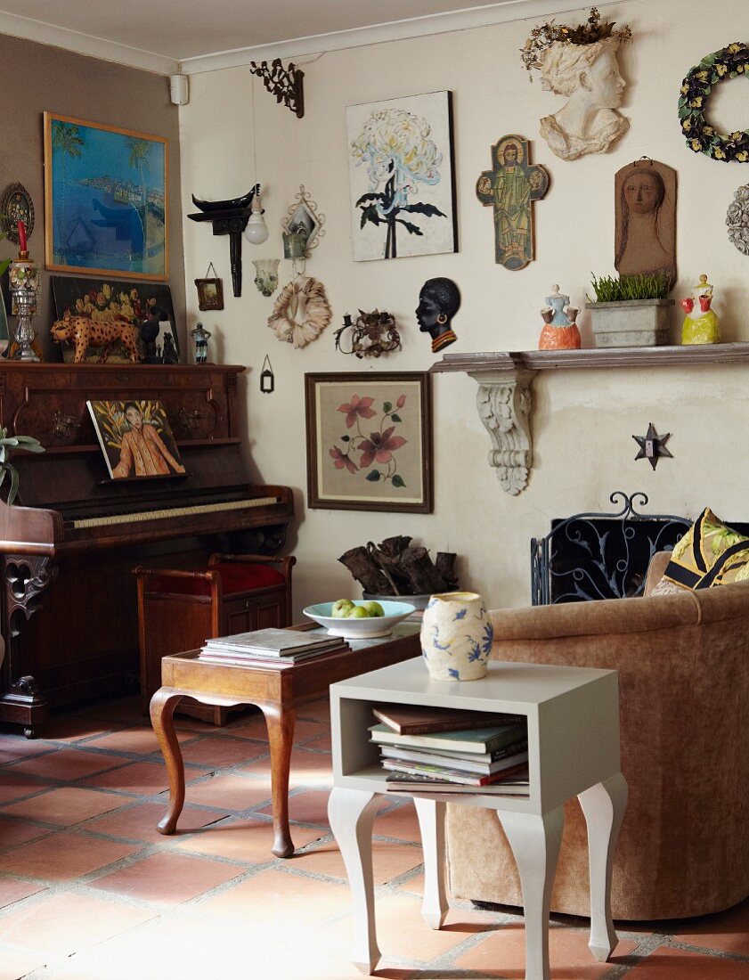 Dekorative Sammelstücke und Bilder an Wohnzimmerwand; darunter ein antikes Klavier und Couch, Couchtisch und Beistelltisch im Vintagelook