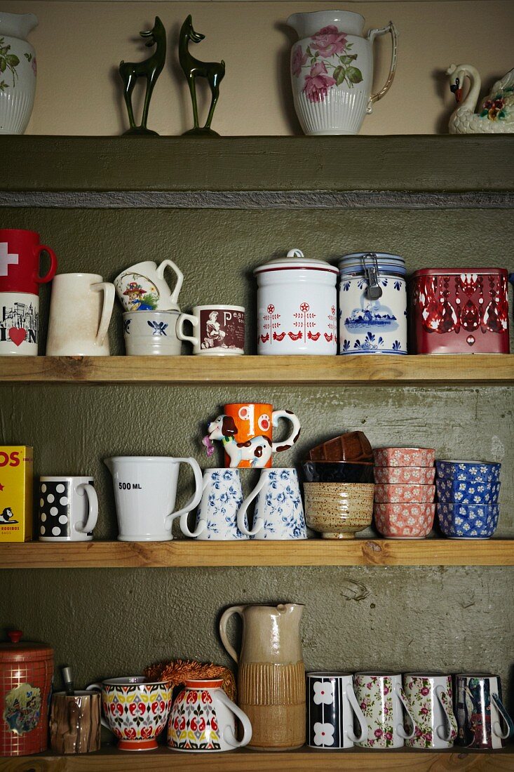 Collection of coffee cups, tea bowls and china jars on simple wooden shelves