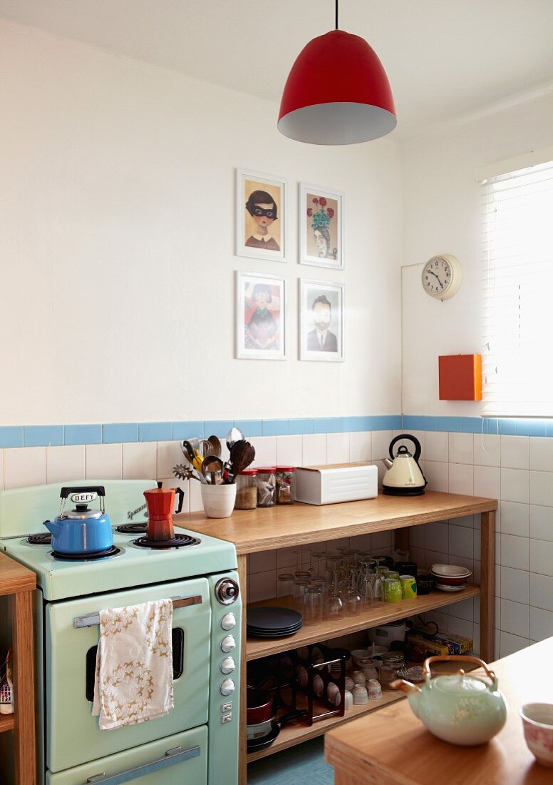 Retro cooker in corner of kitchen with modern, wooden shelves against tiled walls; pendant lamp with red lampshade