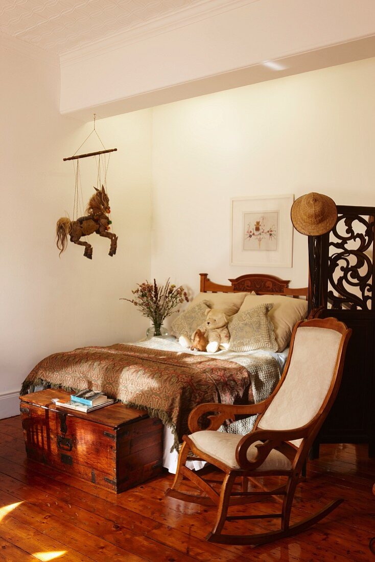 Traditional rocking chair next to wooden trunk at foot of double bed on rustic wooden floor
