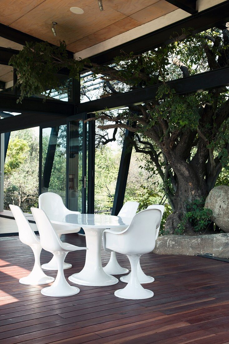 Sitzplatz mit weissen Schalenstühlen im Bauhausstil auf Holzterrasse und Blick in Garten