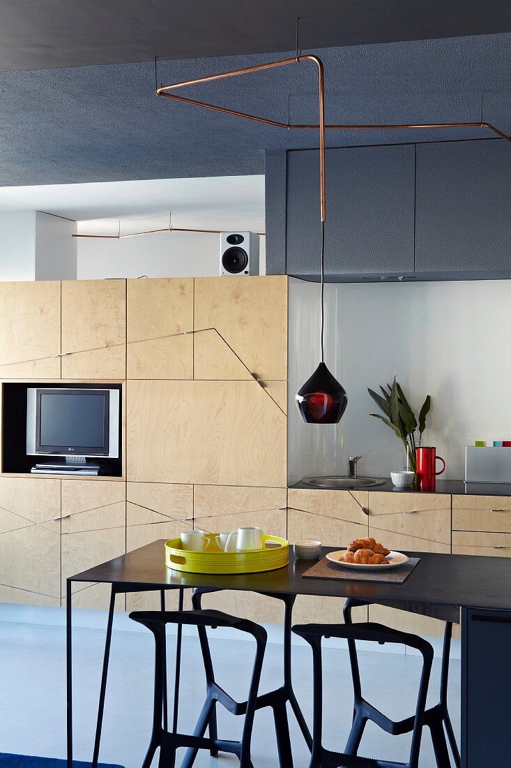 Einbauschrank mit hellen Holzfronten als Verbindung von Wohn- und Küchenbereich in offenem Wohnraum; im Vordergrund eine schwarze Esstheke