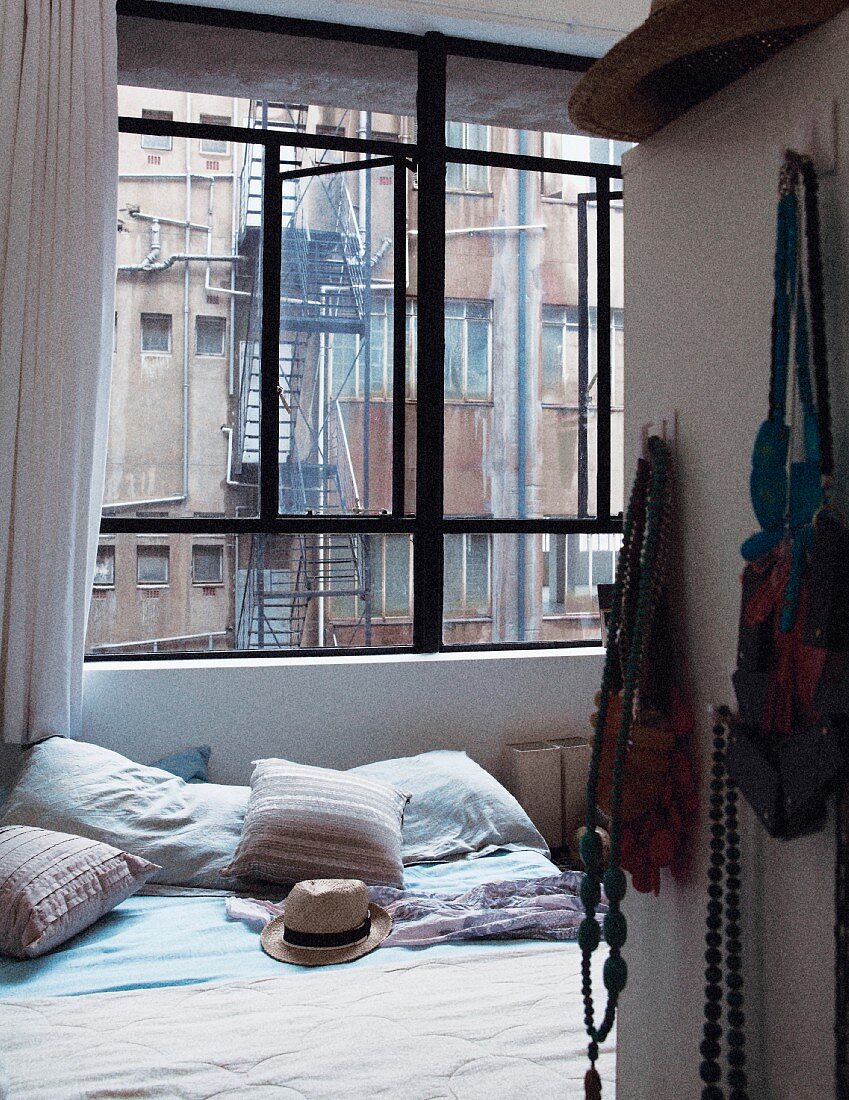 Double bed in bedroom with view of fire escape and windows of neighbouring building through industrial window