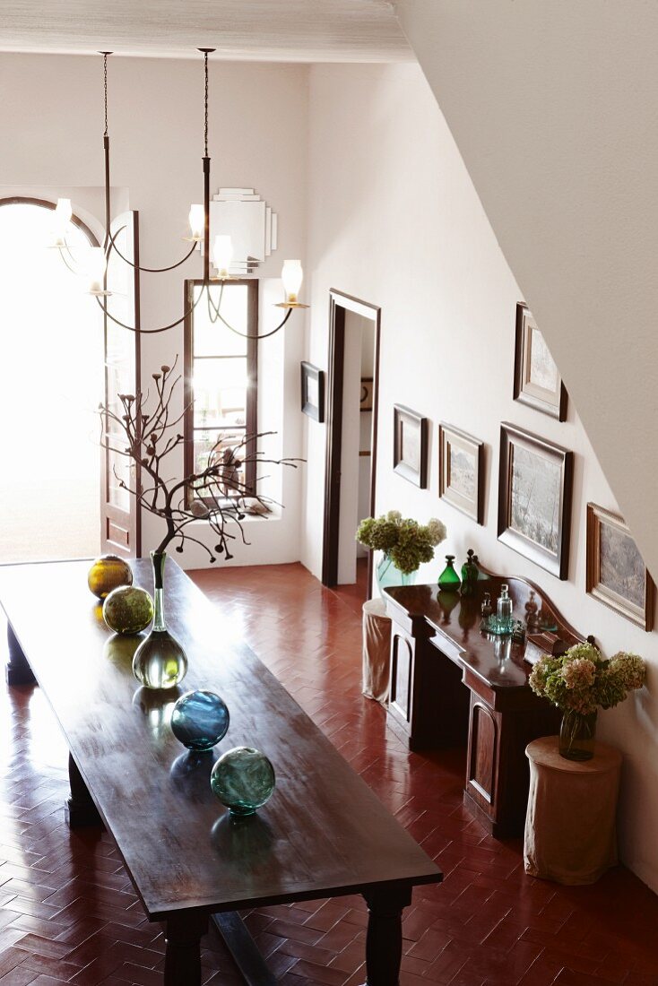 Glaskugelreihe auf langem Holztisch, Vasen mit Trockenpflanzen und Gemäldesammlung in zentraler Wohndiele