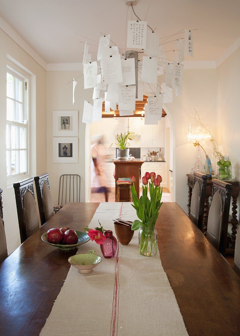 Long wooden dining table with runner of ecru linen and antique chairs; Zettel'z chandelier above table