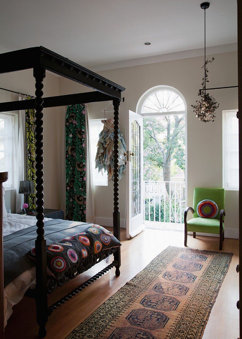 Schwarzes Himmelbett mit kunstvoll gedrechselten Bettpfosten in Schlafzimmer mit offener Balkontür und mit Blick in den Garten