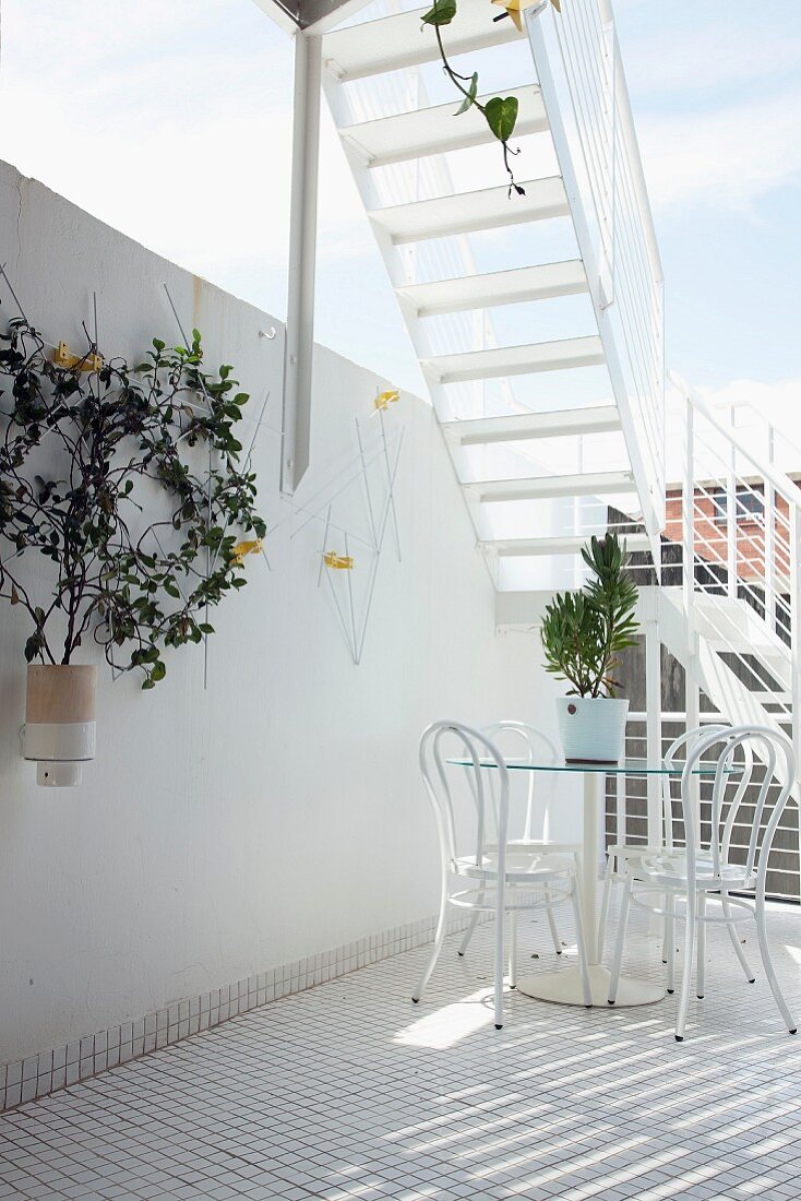 Terrasse mit weißem Mosaikfliesenboden, weisser Sitzgruppe und mit einem Treppenaufgang zur noch höher gelegenen Dachterrasse