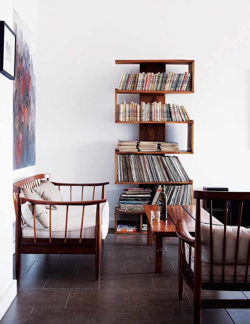 Eigenwillig verwinkeltes Bücherregal an weisser Wand in klarem, hellen Wohnzimmer mit filigranen Holzmöbeln