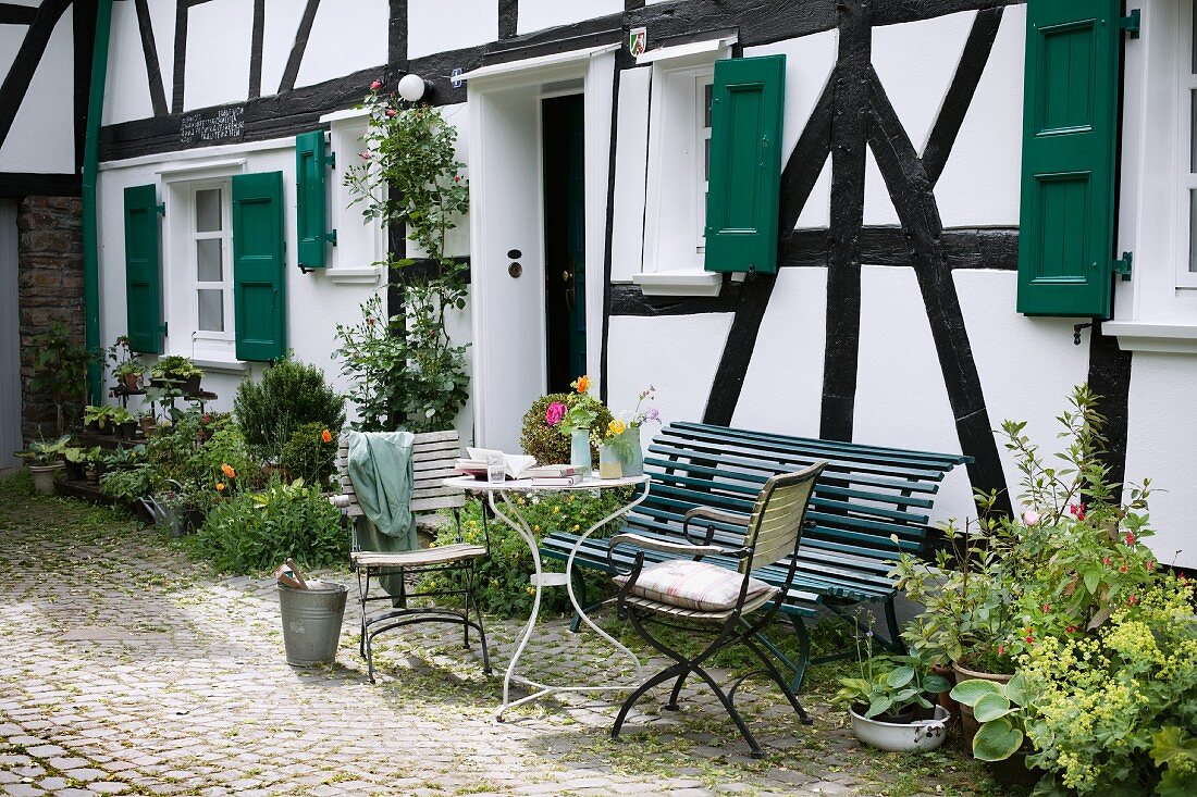 Delicate garden table, garden chairs and bench in front of half-timbered house in summery atmosphere