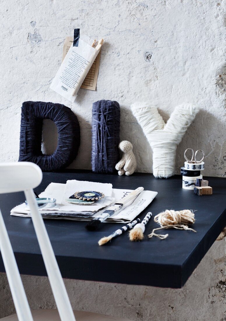 Cardboard letters wrapped in blue and white wool on desk leaing against roughly rendered wall