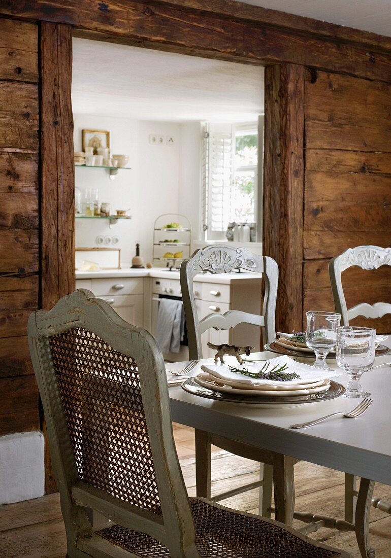 Antique French chairs with grey-painted wooden frames at hand-crafted, Italian dining table in front of open doorway leading to kitchen