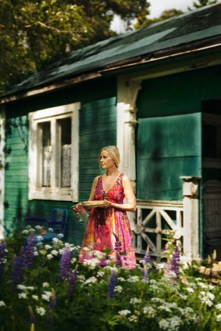 Blonde Frau vor einem Holzhaus in Schweden