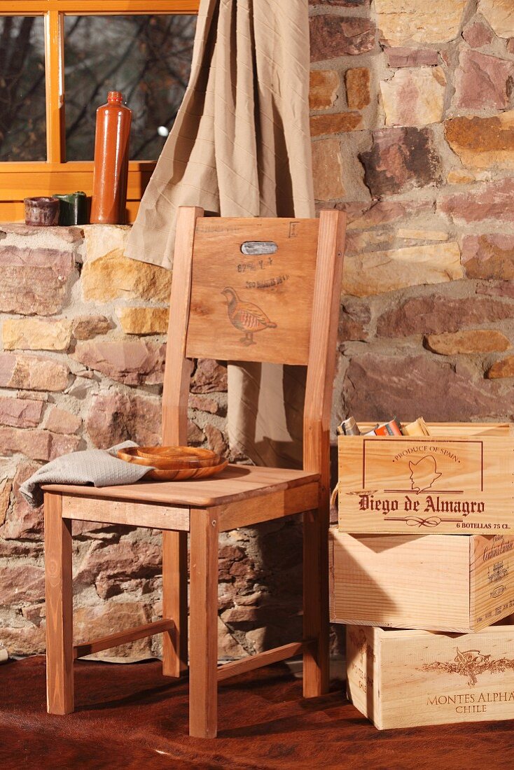 Gestapelte Holzkisten mit Büchern neben Selbstbaustuhl mit Rückenlehne aus der bedruckten Seitenwand einer Weinkiste