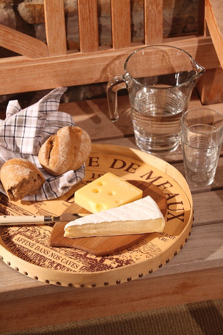 Selbst gefertigtes Käsebrett aus altem Weinkisten mit Spanholzrand; Wasserkaraffe und Gläser auf Holzbank