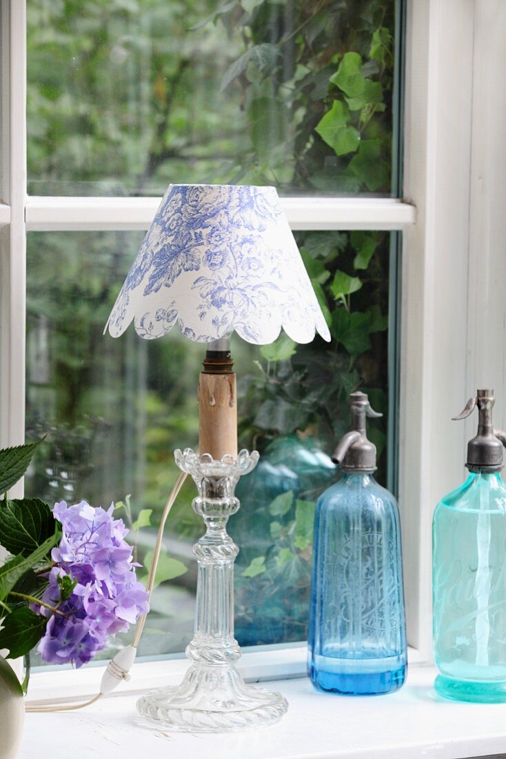 Selbst gefertigter Lampenschirm mit weiss-blauem Toile-de-Jouy Stoff und Vintage Sodaflaschen auf Fensterbank