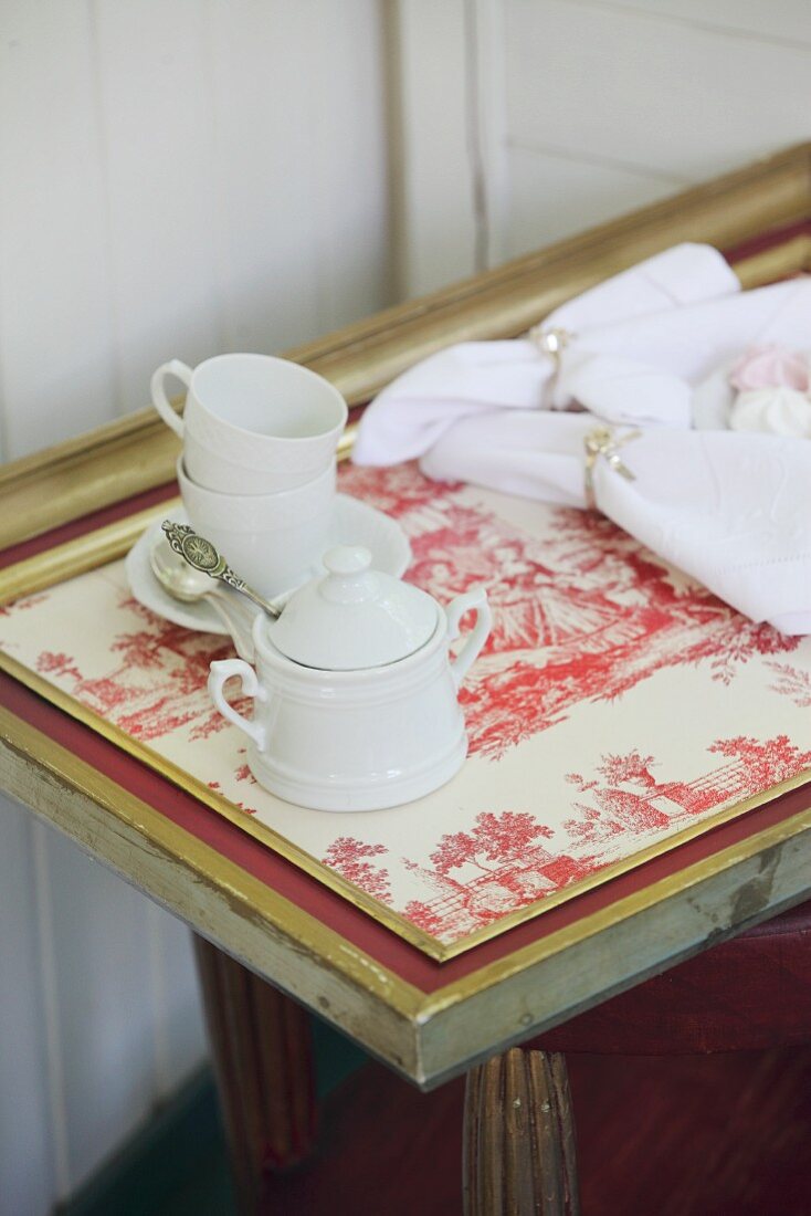 White coffee set on tray covered with red-and-white Toile de Jouy fabric