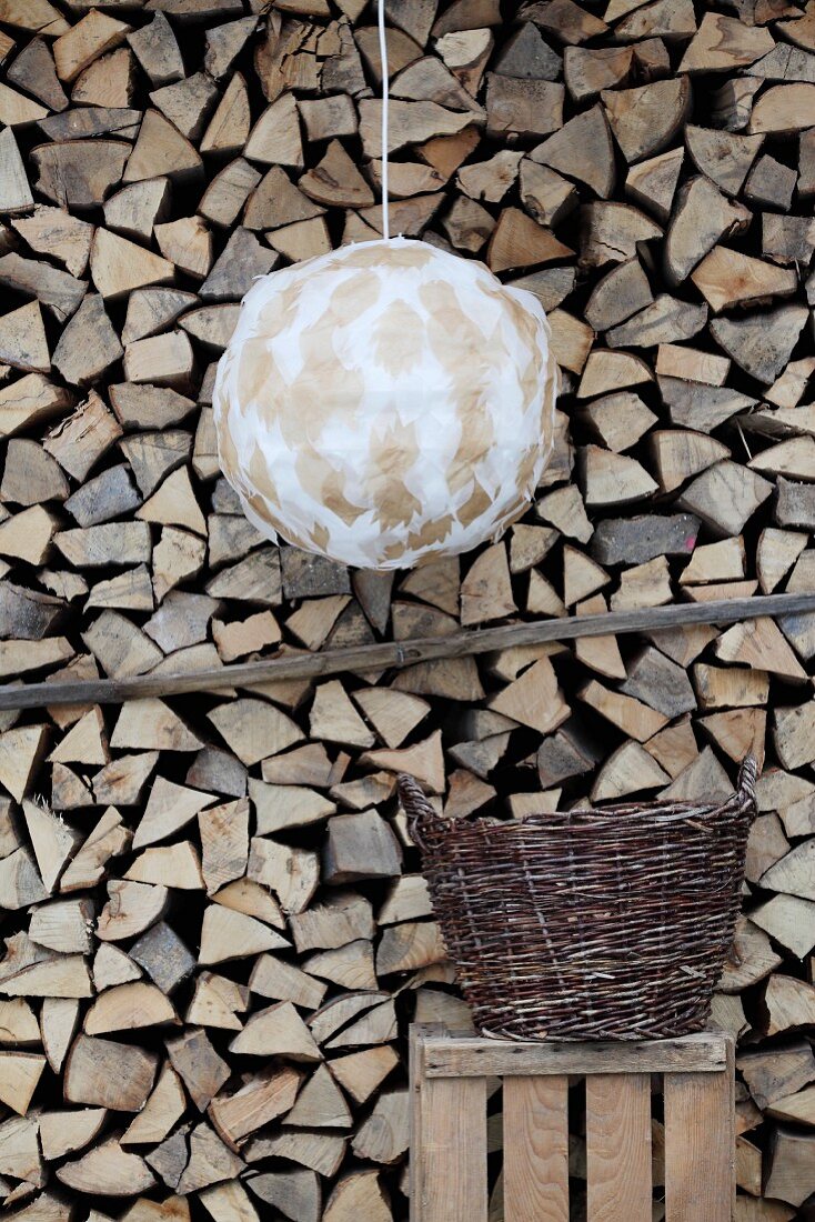 Pendant lamp with hand-crafted spherical lampshade in front of stacked firewood