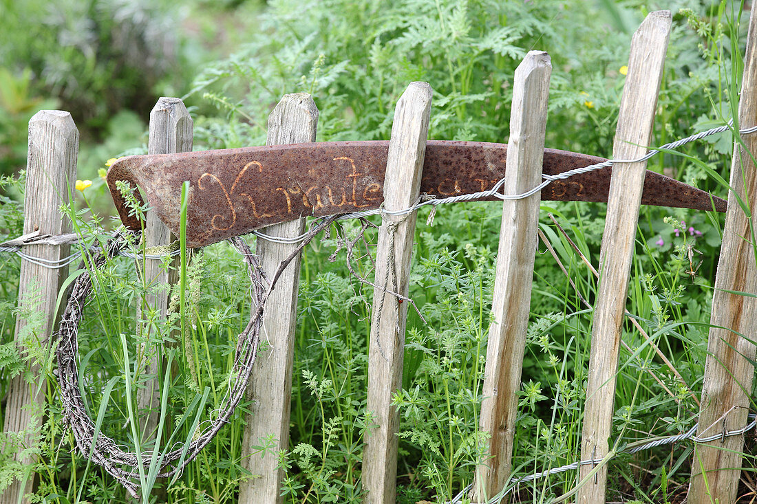 Rusty scythe blade used as sign on paling fence