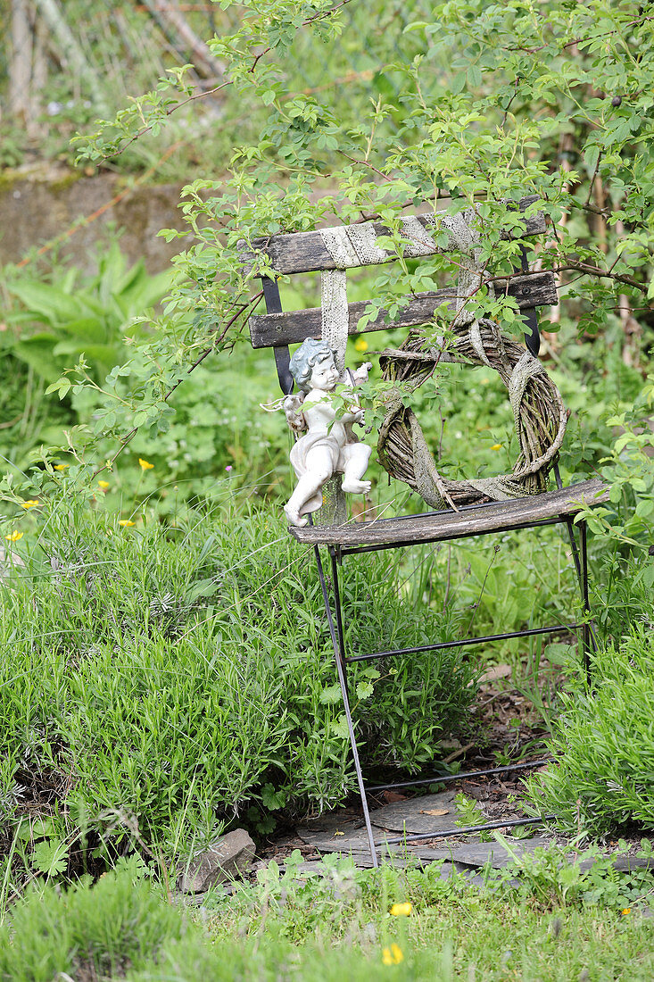 Engelsfigur an einem Weidenkranz auf einem verwitterten Gartenstuhl