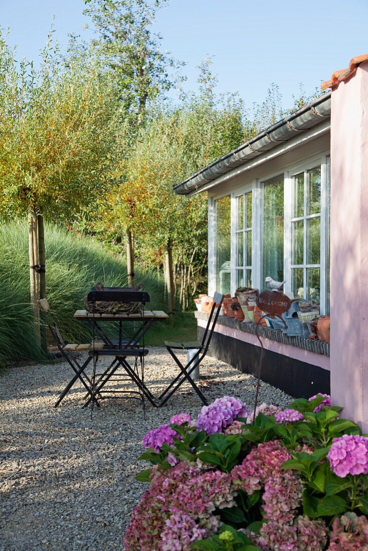 Garden furniture and hydrangea on gravel terrace adjoining glazed extensions of idyllic holiday home