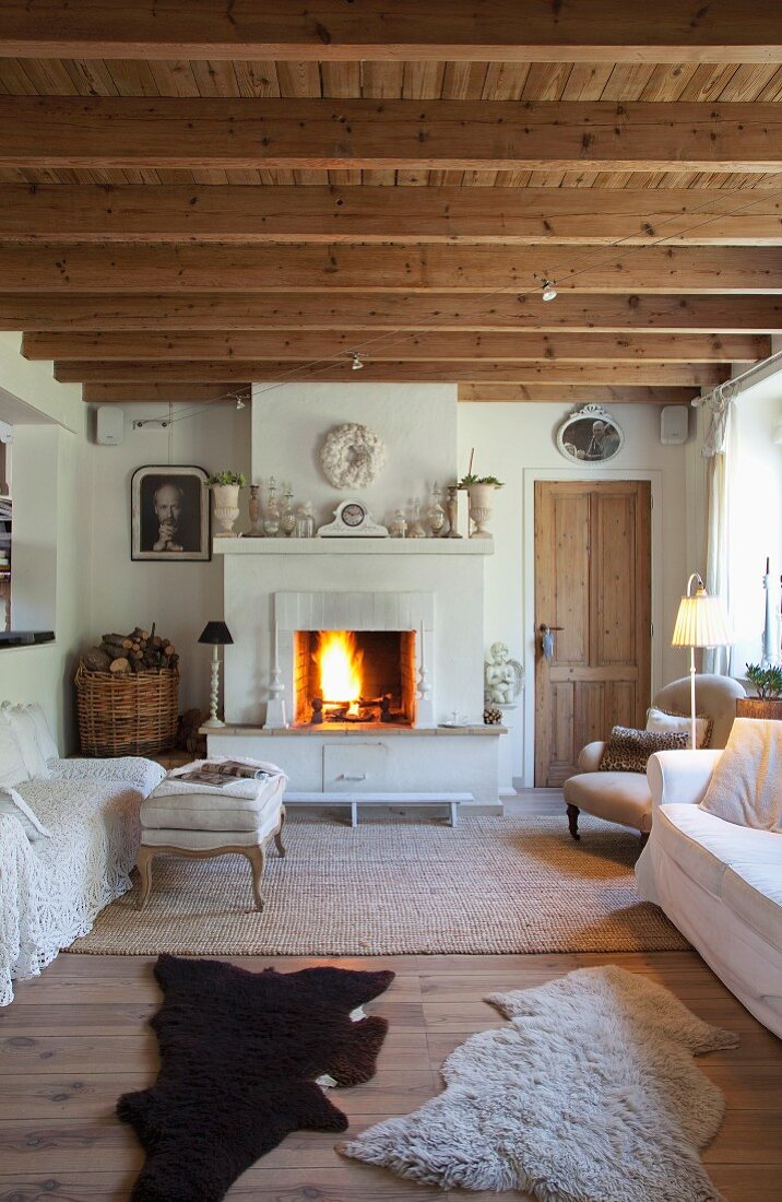 Fellteppiche vor hellen Sofas und Kaminfeuer im gemütlichen Shabby Wohnraum eines belgischen Ferienhauses