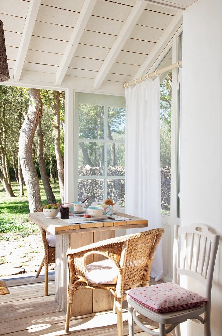 Gedeckter Frühstückstisch mit Korbstühlen im sonnigen Wintergartenanbau eines belgischen Ferienhauses