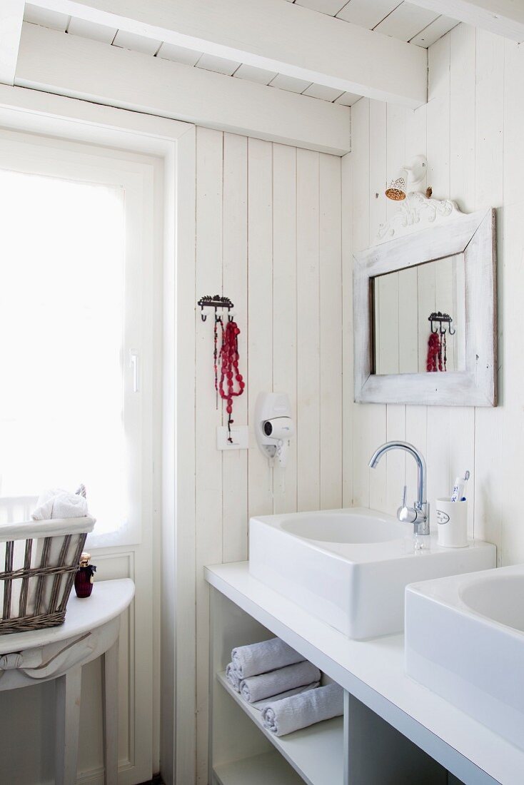 White, shabby-chic bathroom with large countertop sinks on washstand with towel compartments