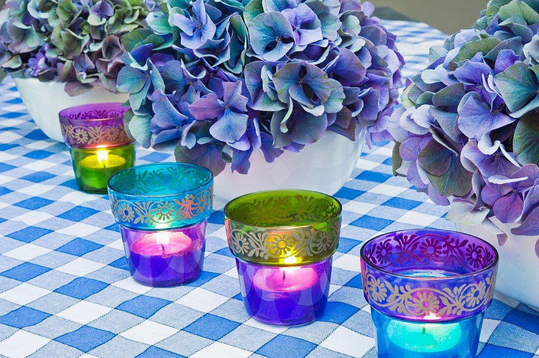 Blaues Stillleben, arrangiert mit Hortensienblüten und romantischen Teelichtern aus farbigem Glas