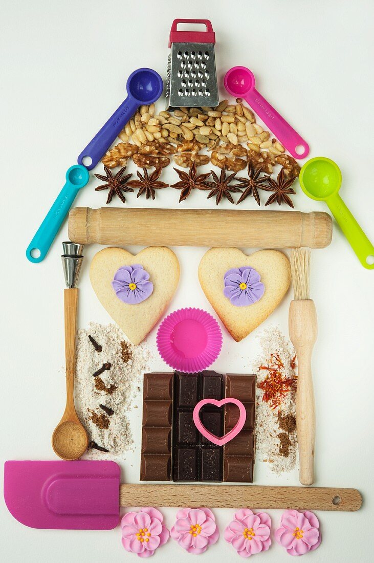 Backutensilien, Gewürze, Schokolade und fertige Kekse in Form eines Hauses drapiert