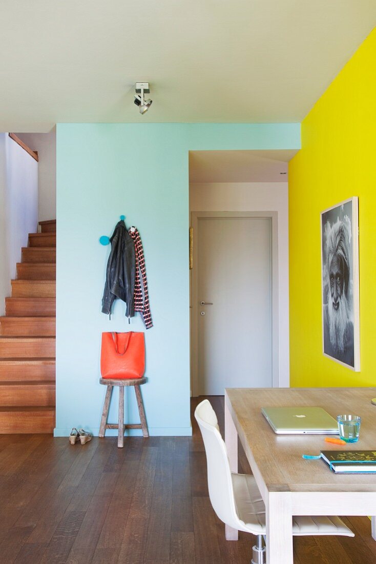 Office area in hallway of colourful apartment with coat pegs on wall and foot of wooden staircase