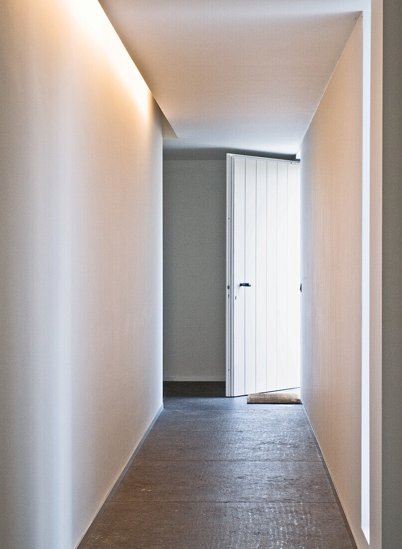 Narrow hallway with indirect lighting and white door at the end