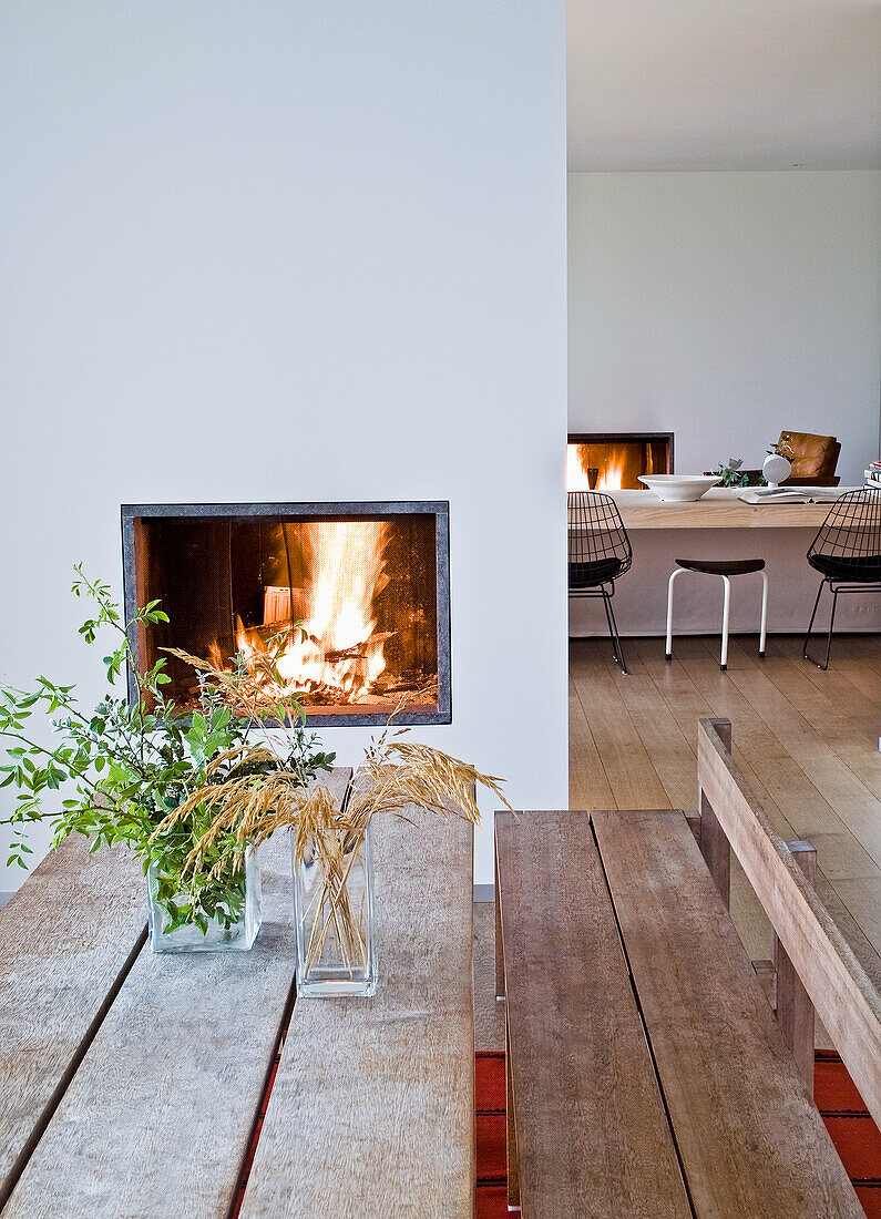 Esstisch aus Holz mit Pflanzen in Vasen, Kamin im Hintergrund