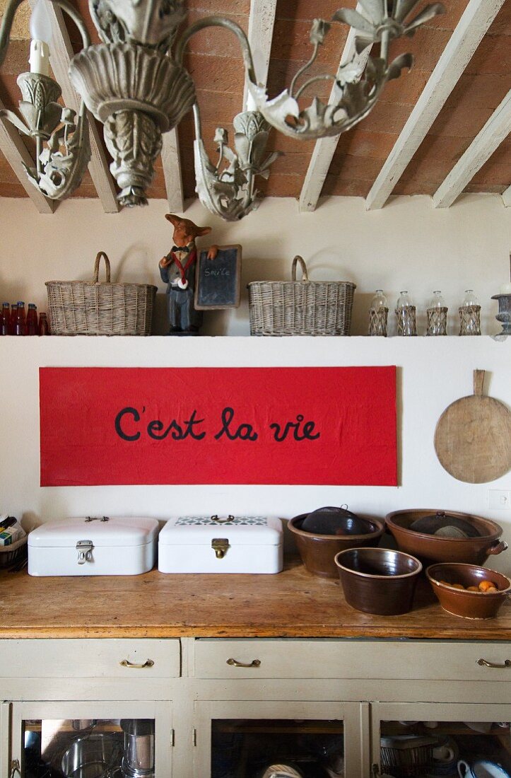 weiße Emaillebrotkästen und Tonschüsseln auf rustikaler Küchenarbeitsfläche; Sinnspruch auf rotem Papier