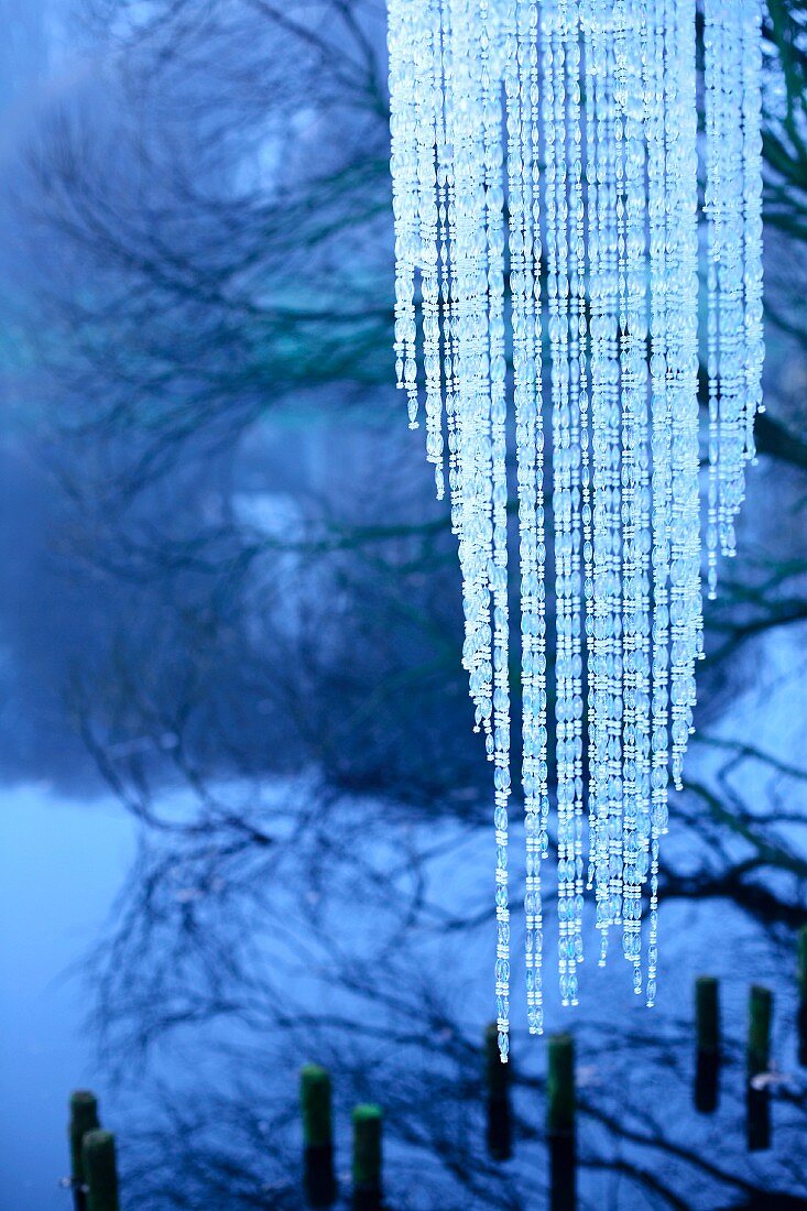Pendant lampshade made from strings of beads on shore of lake in wintery dawn light