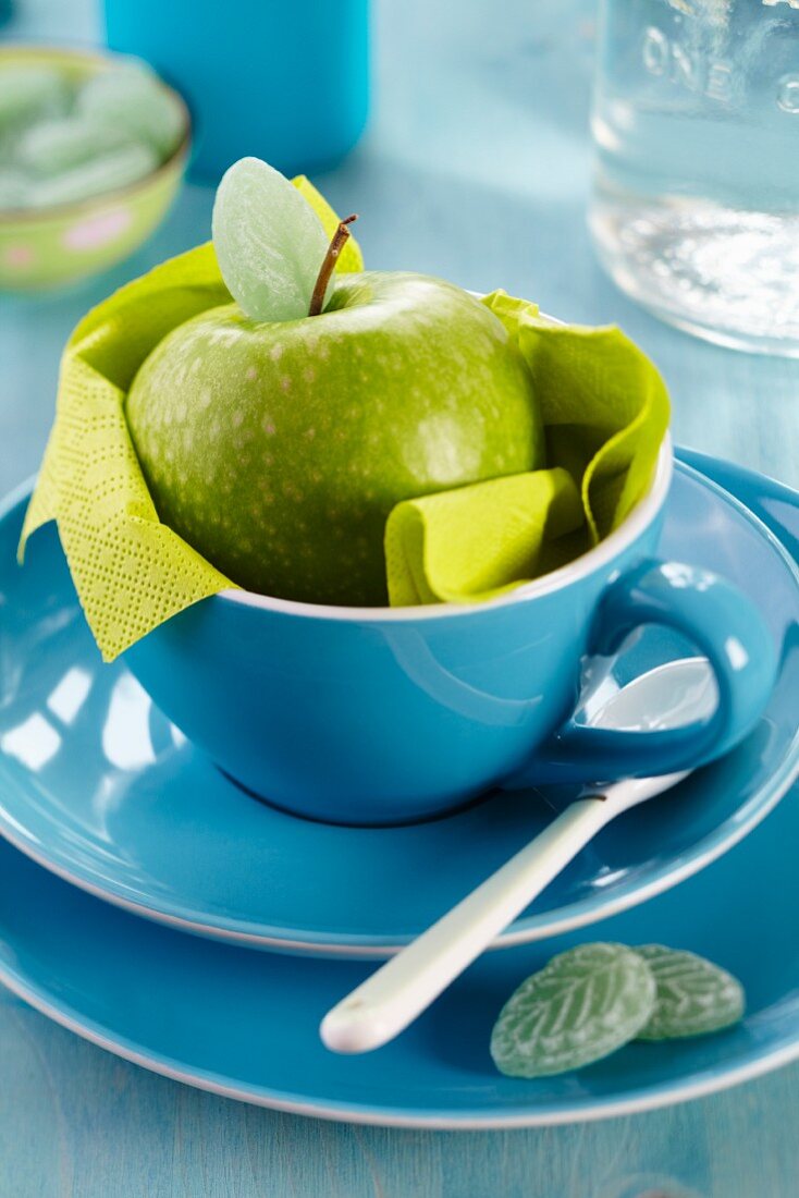Grüner Apfel mit blattförmigem Bonbon in blauer Tasse