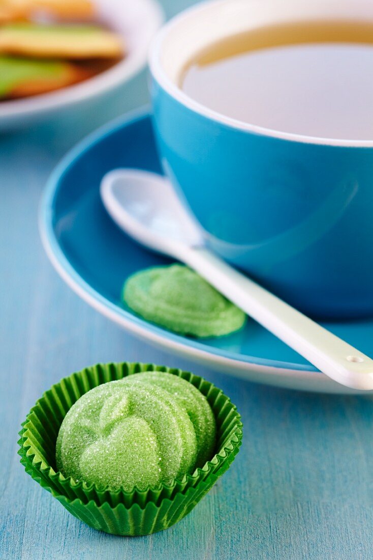 Grüne Zuckerplättchen mit Apfelrelief in Minimuffinform vor Teetasse