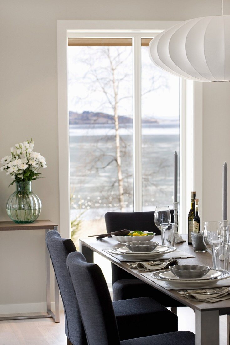 Dark blue upholstered chairs around festively set dining table in front of French doors with view of Norwegian skerry coast
