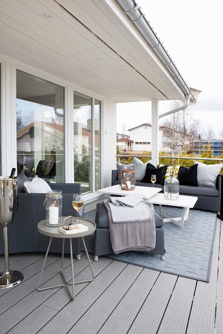 Graue Polstermöbel mit Beistelltischen und Teppich auf Balkon vor der Fensterfront eines skandinavischen Holzhauses