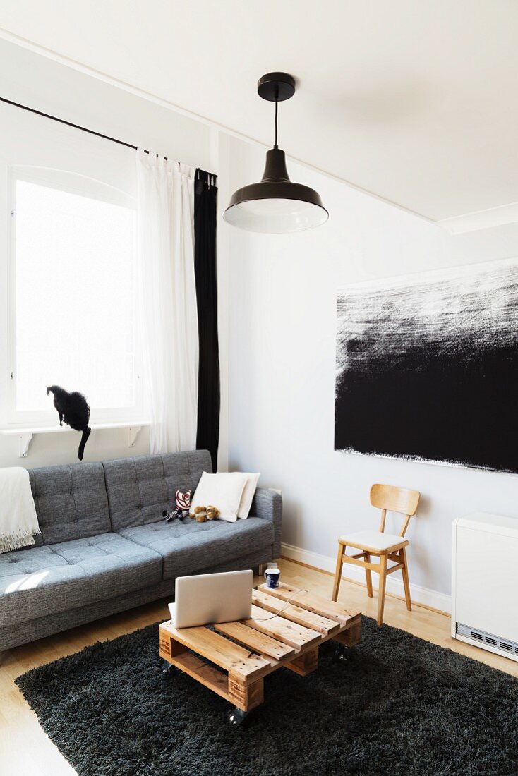 Holzpalette als Couchtish vor Sofa und modernes schwarz-weisses Bild aus Stoff an der Wand