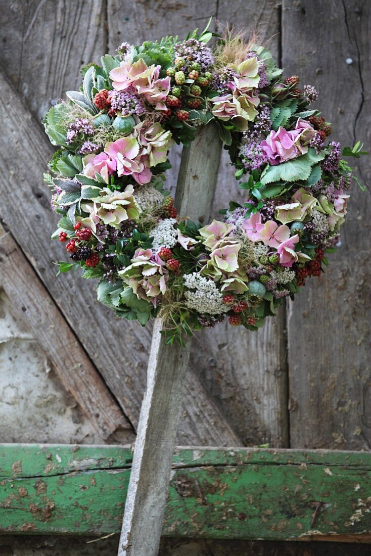Mit Hortensienblüten und Beerenzweigen gestalteter Blumenkranz auf einer Holzlatte