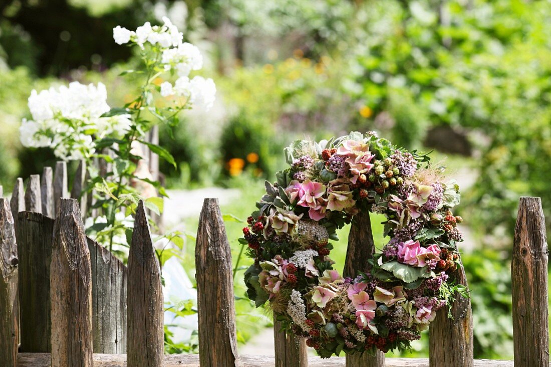 Mit Hortensienblüten und Beerenzweigen gestalteter Blumenkranz auf Staketenzaun