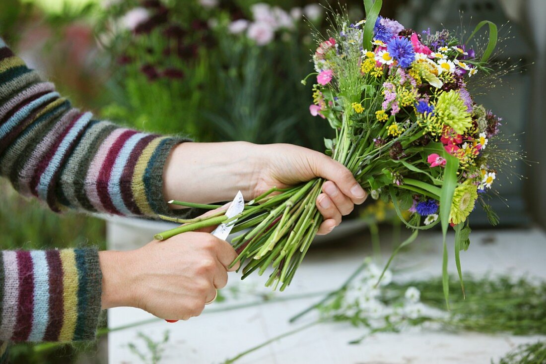 Floristenhände beim Kürzen der Stengel eines sommerlichen Blumenstrausses