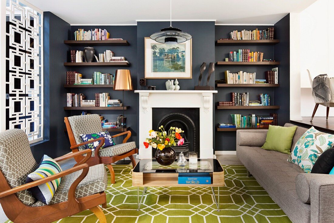 Gepolsterte Armlehnsessel und schlichtes Sofa auf olivgrünem Teppich mit Wabenmuster; seitlich ein Metallgitter als Raumteiler
