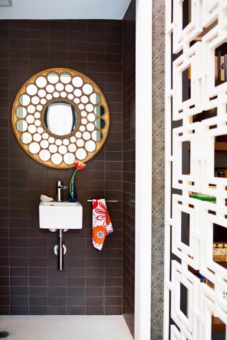 Mini-Handwaschbecken und ornamentaler, runder Spiegel auf braunen Riemchenfliesen, ergänzt mit einem Blumenmuster Handtuch