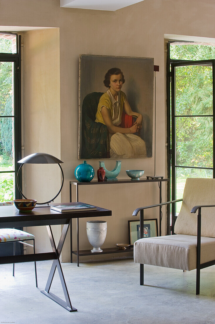 Raum mit Deko, Tisch, Sessel, Gemälde und Blick ins Grüne